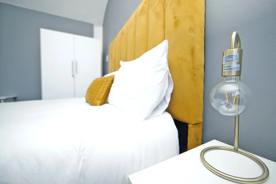 Close view of the bed, yellow headboard and bedside lamp